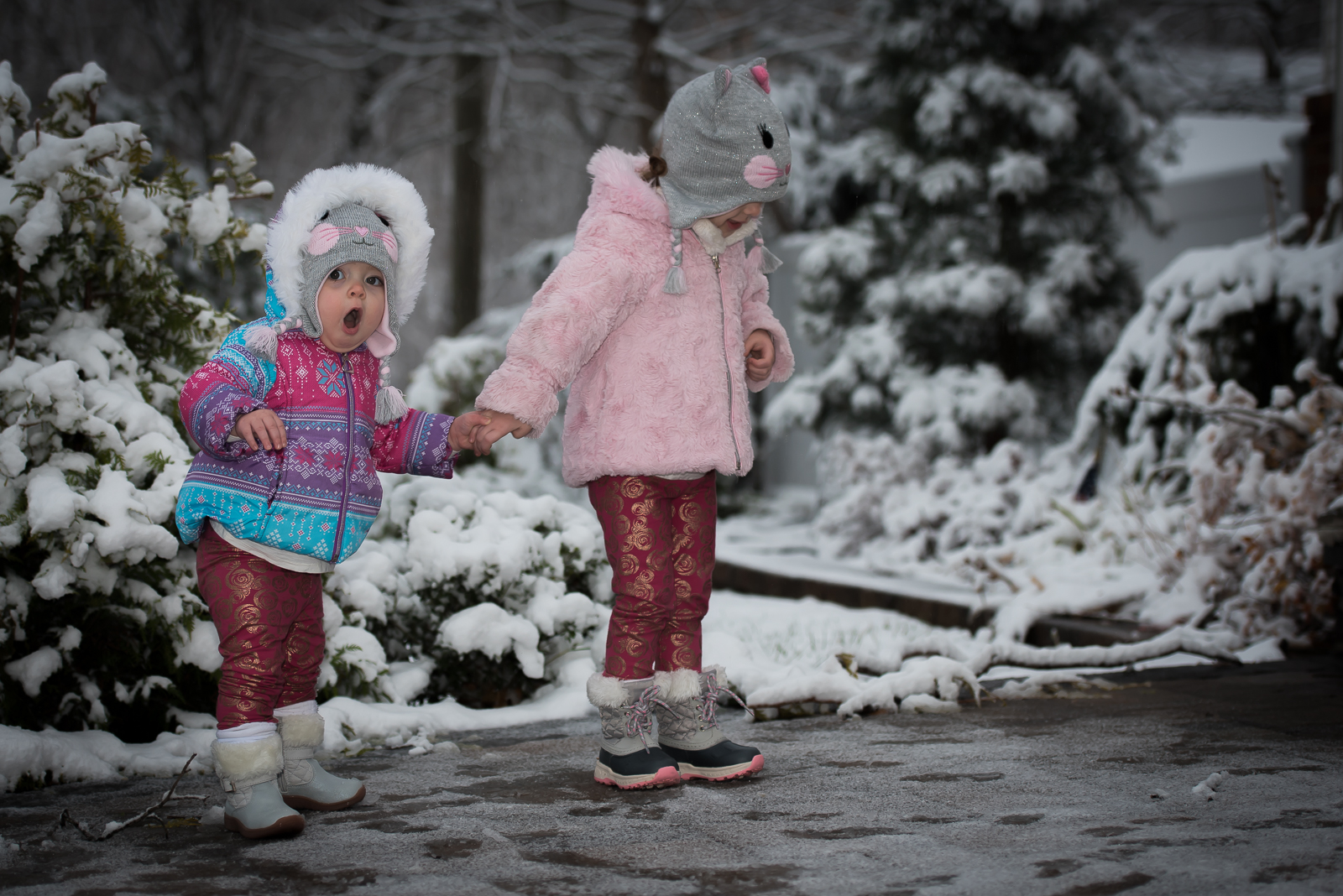 Two children in winter clothing holding hands in snow